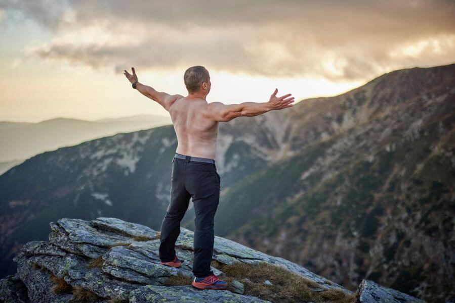Középkorú férfi áll a hegytetőn széttárt karokkal